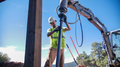 Construction worker handling equipment beside an excavator on a clear day.