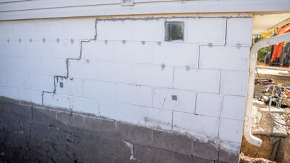 Cracked white foundation wall with visible repair work and a small glass block window.