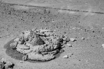 Pile of wet cement on a concrete surface, creating a textured mound, in a black and white photograph.
