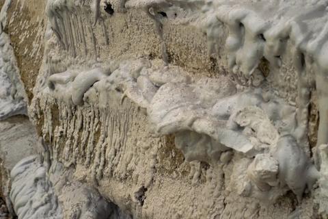 Thick, grayish-white mud or clay dripping and drying on a rough wall surface.