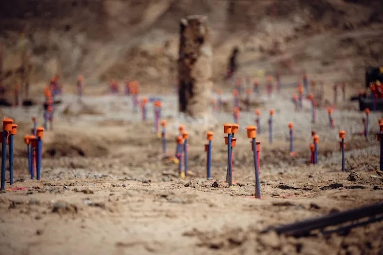 Numerous survey stakes with orange caps are placed in dry, rocky soil at a construction site.