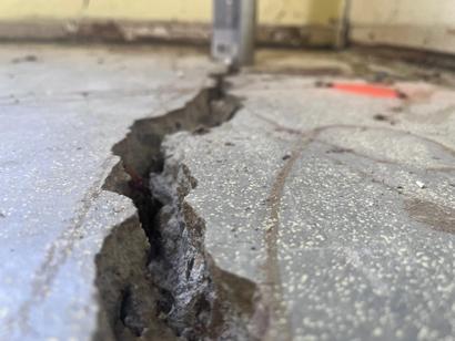 Close-up of a large crack in a concrete floor near a wall, indicating structural damage.