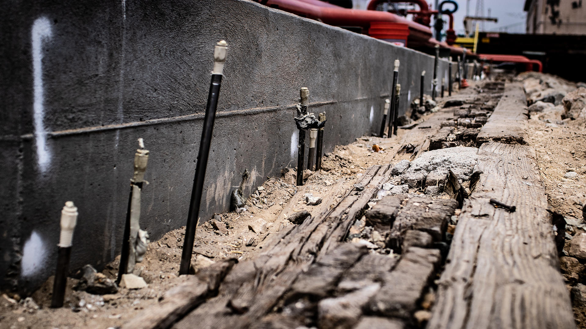 Exposed rebar and weathered wooden planks next to a concrete wall at a construction site.