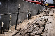 Exposed rebar and weathered wooden planks next to a concrete wall at a construction site.
