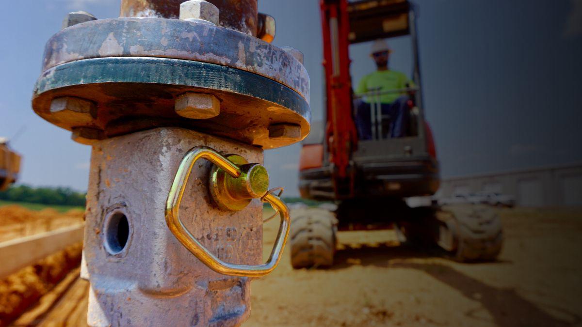 Close-up of construction equipment part with a worker on machinery blurred in the background at a worksite.