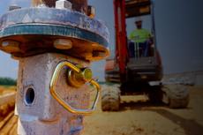 Close-up of construction equipment part with a worker on machinery blurred in the background at a worksite.