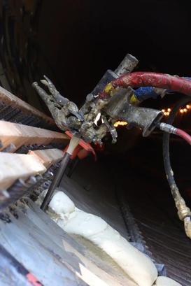 Close-up of a construction tool applying foam or sealant inside a tunnel or pipe with wiring visible.