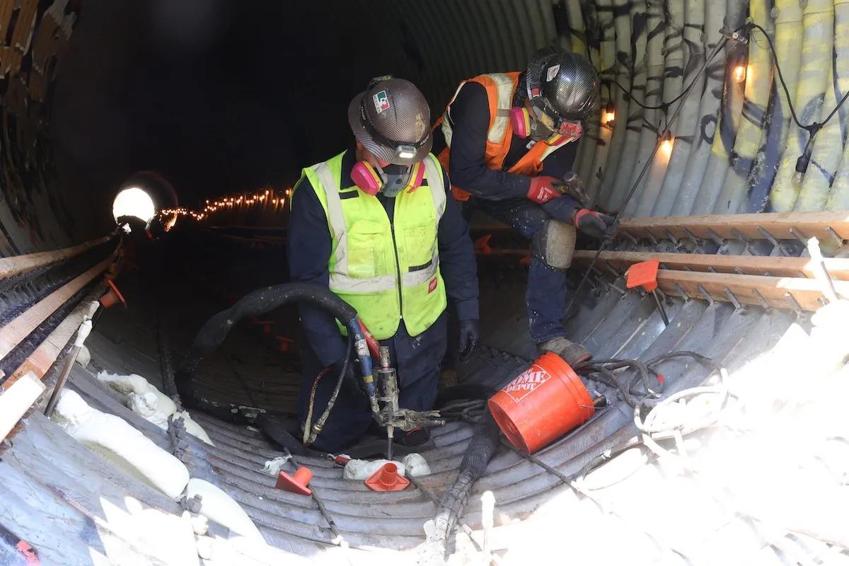 Two construction workers in safety gear work inside a tunnel, using tools near rebar and concrete. Culvert Rehabilitation with Polyurethane
