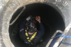 A worker in safety gear descends into a large, circular manhole using a rope and ladder.