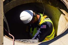 Worker in safety gear with a US flag patch descends into a manhole for maintenance or inspection.