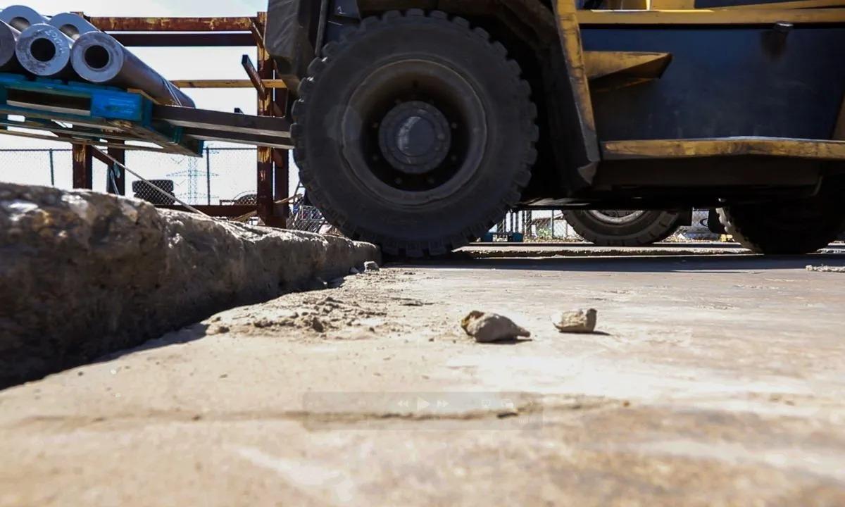 Close-up of a forklift driving over a rough, uneven concrete surface at an industrial site.