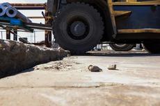 Close-up of a forklift driving over a rough, uneven concrete surface at an industrial site.