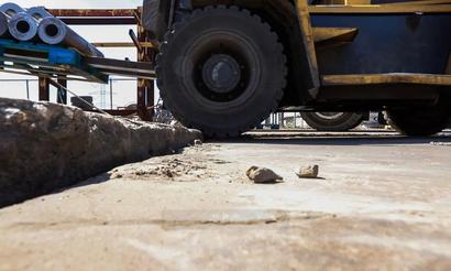 Close-up of a forklift driving over a rough, uneven concrete surface at an industrial site.
