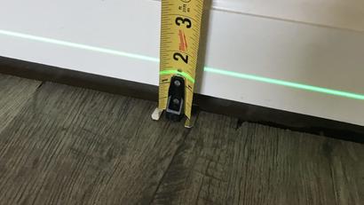 A tape measure shows 2 inches next to a wall above a green laser line on a wood floor.