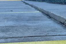 A sidewalk curb next to an empty parking lot with yellow painted lines.