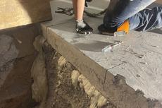 Person kneeling on concrete, working near a large crack filled with spray foam insulation below.