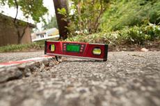 A digital level placed on cracked concrete shows the surface is uneven, with greenery in the background.