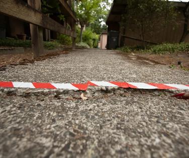 A cracked, raised sidewalk marked with red and white caution tape in a residential area.