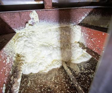 White foam insulation is sprayed between steel beams, expanding and hardening to fill the space.