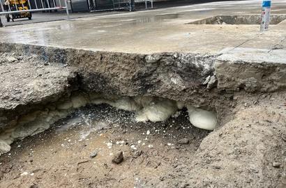 A concrete slab with a large hole beneath it, exposing soil and foam-like material under the surface.