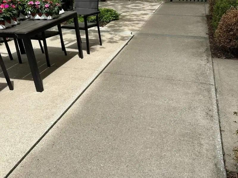 A patio table with potted flowers sits next to a slightly raised concrete sidewalk.