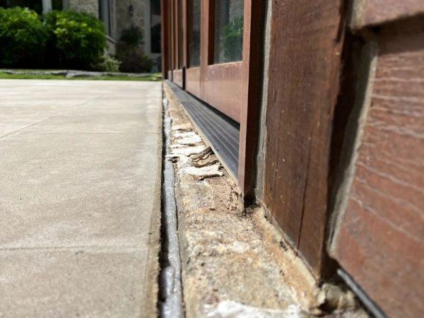 Close-up of a building's wooden door with visible cracks and damage along the concrete foundation.