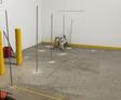 Six metal rods are installed upright in a concrete floor near a step ladder, with yellow bollards at the side.