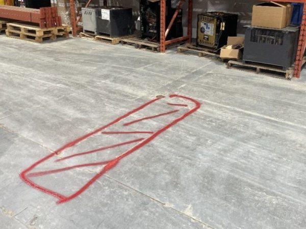 Red spray-painted rectangle with diagonal lines on a warehouse floor near pallets and boxes.