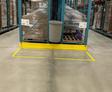 A person stands on a trash can between warehouse shelves with pallets and boxes in the background.