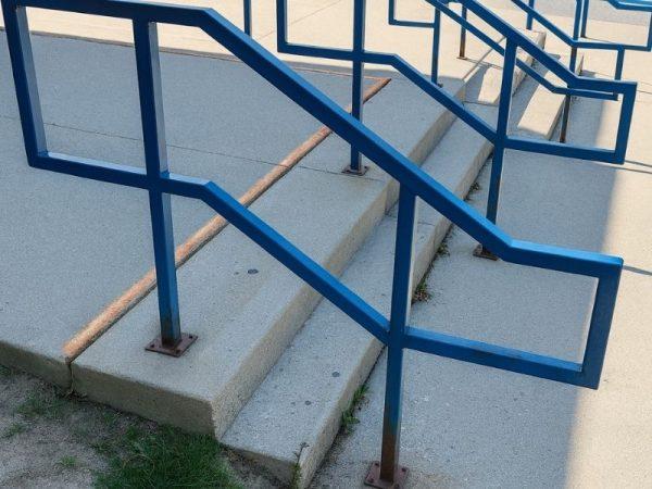 Blue metal handrails with sharp angles along concrete outdoor steps.