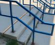 Blue metal handrails with sharp angles along concrete outdoor steps.