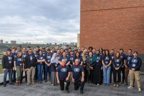 A large group of people pose together outdoors, many wearing matching navy blue event t-shirts.