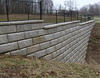 Stone retaining wall with a black metal fence on top, nestled amidst lush grass and towering trees, showcasing its strength yet hinting at the occasional need for attentive retaining wall repair to maintain its timeless elegance.