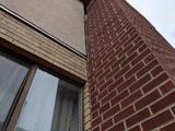 Upward view of a building corner with brick and stucco walls next to a window.