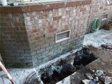 Brick wall with soil removed, showing foundation repair using hydraulic jacks. Garden hose on the side.