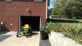 Lawn mower in front of a brick garage beside a grassy yard with trees.