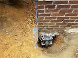 Foundation repair with hydraulic jack beside brick wall and exposed soil.