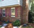 Brick house with red shutters and garden work in progress, including soil piles and tarp.