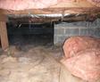 A crawl space with exposed pink insulation and a dirt floor.