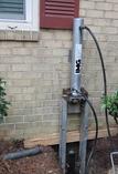 A hydraulic jack system is set up next to a brick house wall for foundation repair.