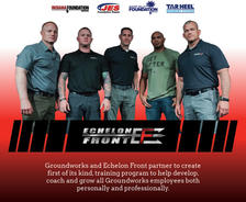 Five men standing together in front of a white background with logos, wearing black and gray shirts.