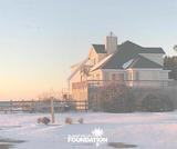 A large house with a snowy yard at sunset, featuring a wooden deck and a logo in the bottom corner.