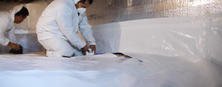 Two workers in protective suits install a vapor barrier in a crawl space.