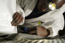 Person in protective suit and headlamp working with tools under a surface.