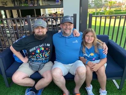 A man and two children sitting on a bench, smiling, outdoors near a fenced area.