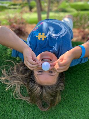 Child upside down on grass, smiling, holding a ball on their nose.