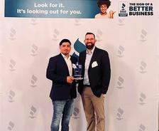 Two men holding an award stand in front of a BBB backdrop with the slogan "Look for it. It’s looking out for you.