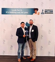 Two men holding an award stand in front of a BBB backdrop with the slogan "Look for it. It’s looking out for you.