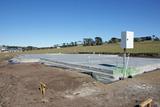 Concrete foundation slab in an open field with clear blue sky and distant trees.