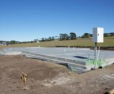 Concrete foundation slab in an open field with clear blue sky and distant trees.